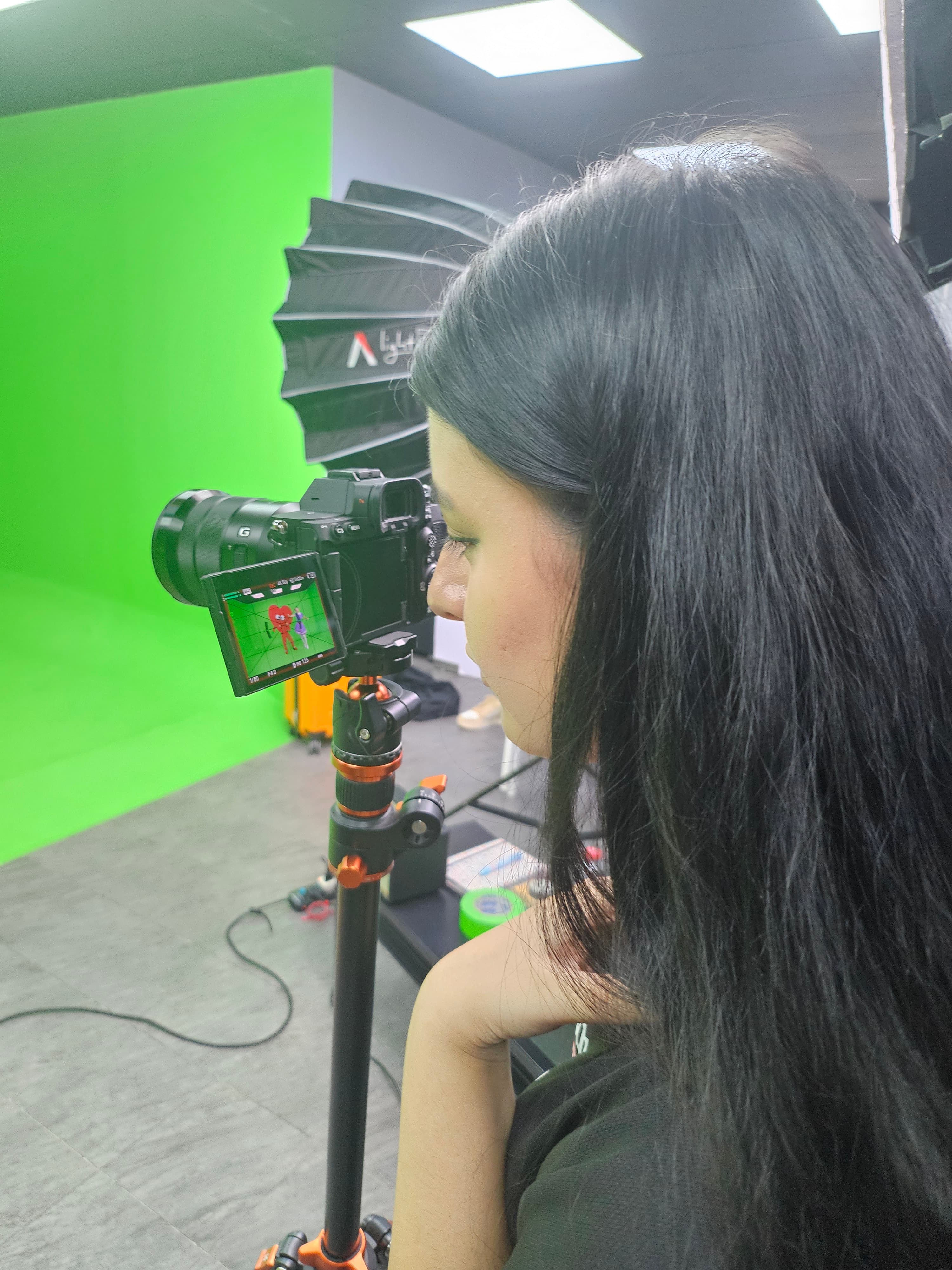 Woman with long black hair looks at a camera screen in a green screen studio.