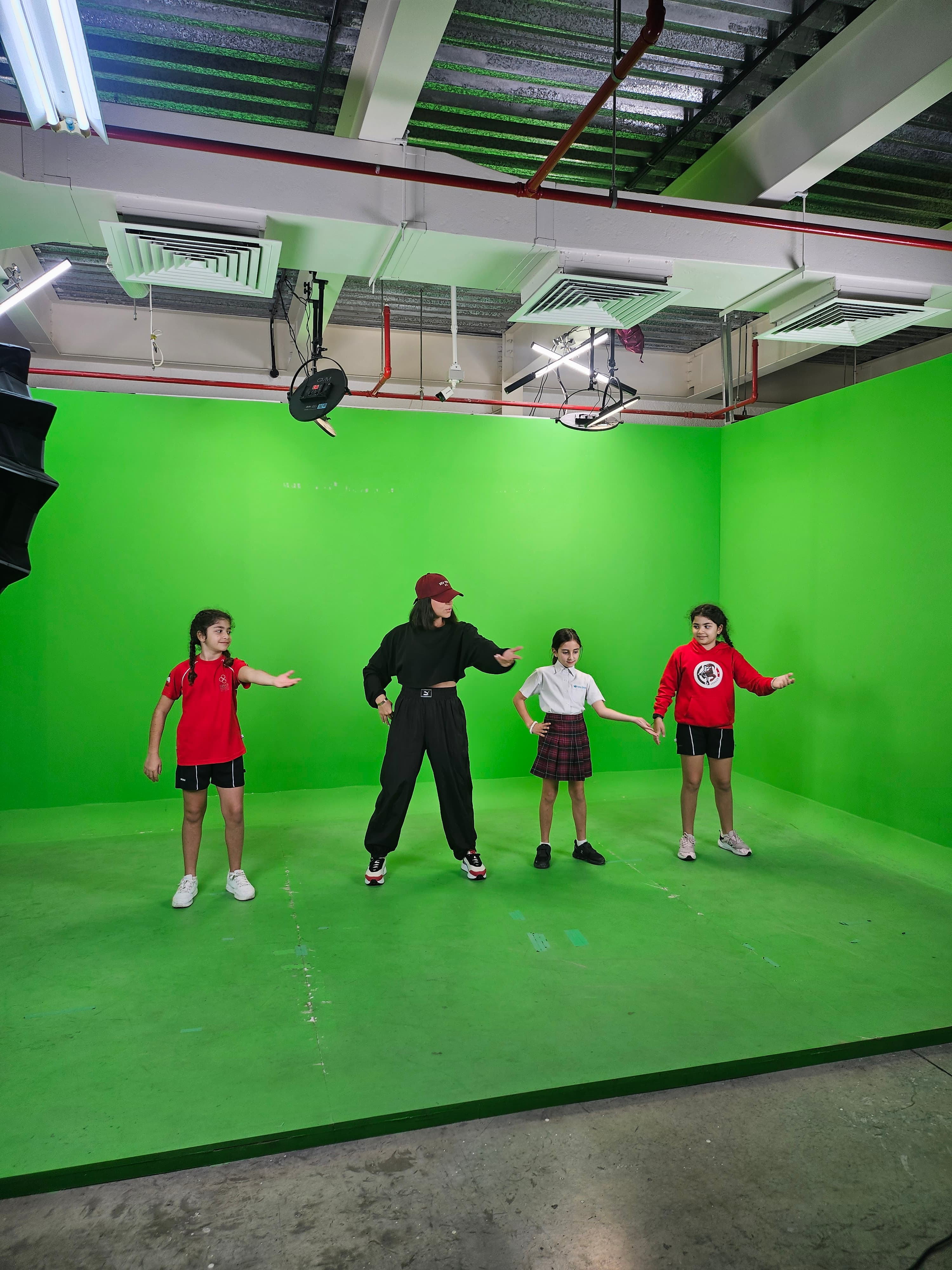 Four people in red, white, and black outfits pose inside a green screen studio.